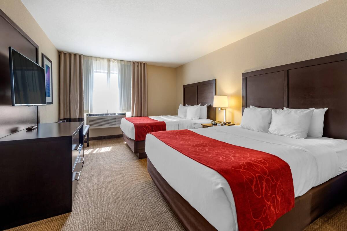 A hotel room with two beds, a desk, a TV, and a window with curtains.