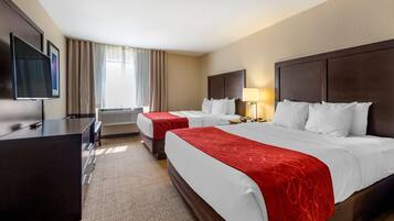 A hotel room with two beds, a desk, a TV, and a window with curtains.