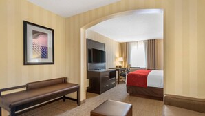 A hotel room with a bed, a desk, a television, a bench, and a sofa.