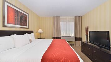 A hotel room with a large bed, a flat-screen TV, a dresser, a lamp, and a window with curtains.