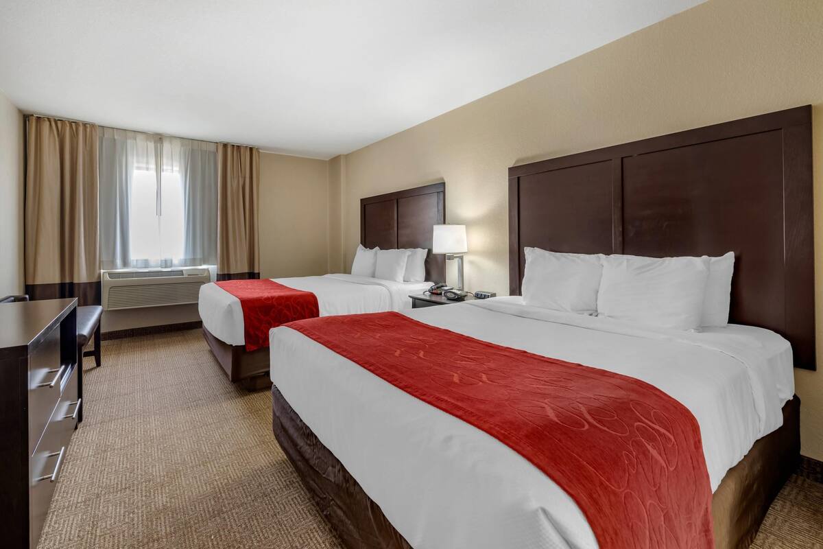 A hotel room with two beds, a desk, a lamp, and a window with curtains.