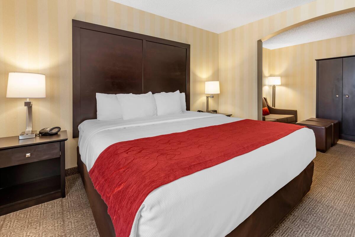 A hotel room with a large bed, two bedside tables, a nightstand, a wardrobe, and a mirror.