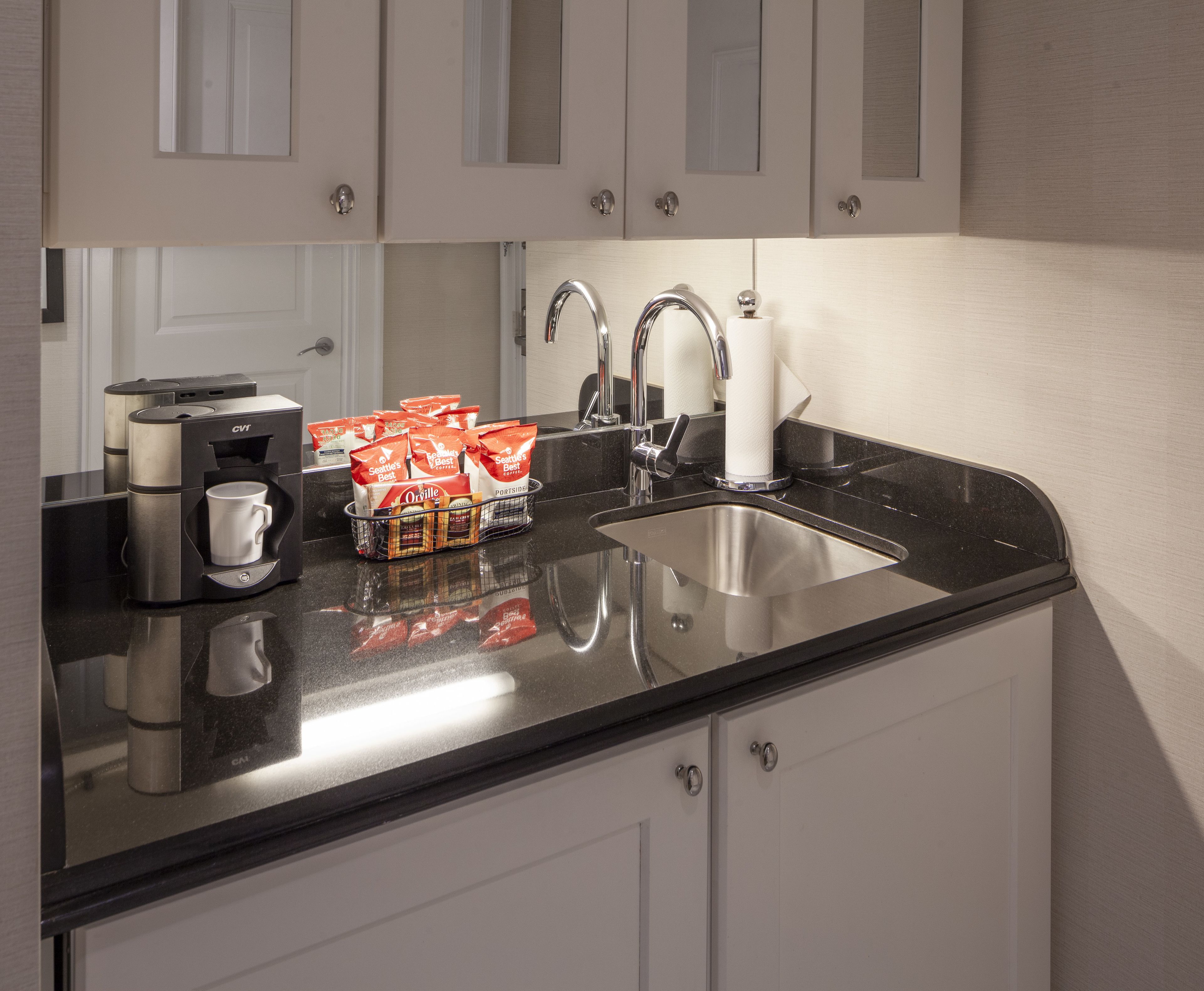 A modern kitchen with a black countertop, stainless steel sink, and white cabinets.