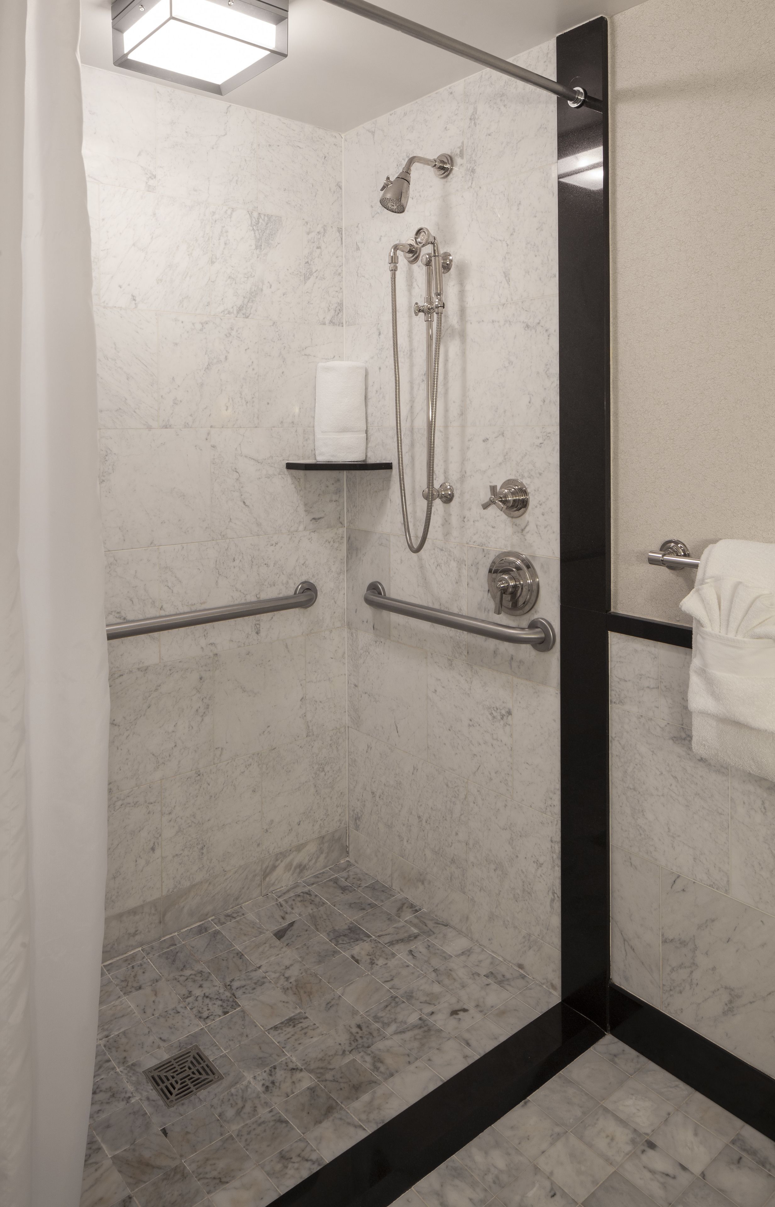 A modern shower area with a glass door, marble walls, and a black accent strip.