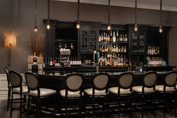 A modern living room with a glass table, leather chairs, a sofa, and a coffee table. There are two lamps, a framed picture on the wall, and a window with a city view. at The Manhattan Club