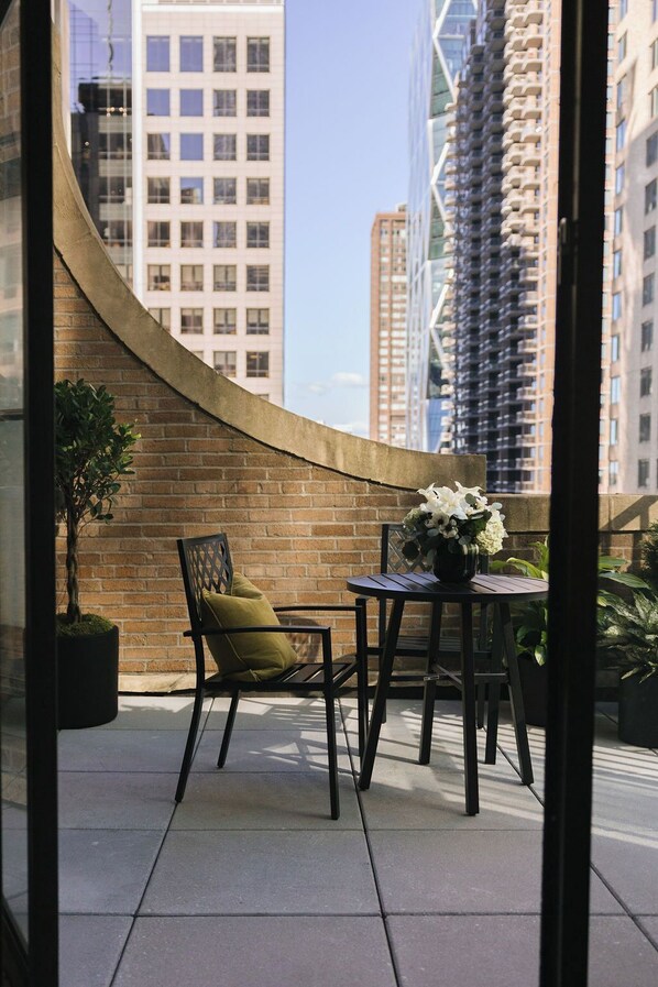 A balcony with a brick wall, a potted plant, a chair, and a table with a vase of flowers.