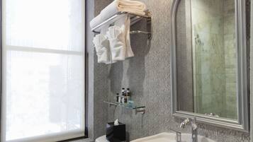 A bathroom with a toilet, sink, and large mirror. There is a window with a view of buildings, and towels are hung on a rack.