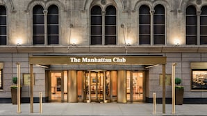Manhattan Clubin sisäänkäynti, jossa on kivijulkisivu, kaarevat ikkunat ja kultaisilla kirjaimilla varustettu kyltti.