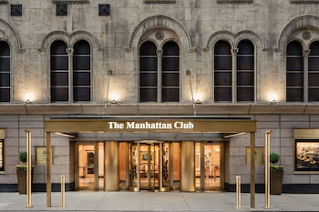 A hotel room with a large bed, a desk, a chair, and a window with curtains. at The Manhattan Club