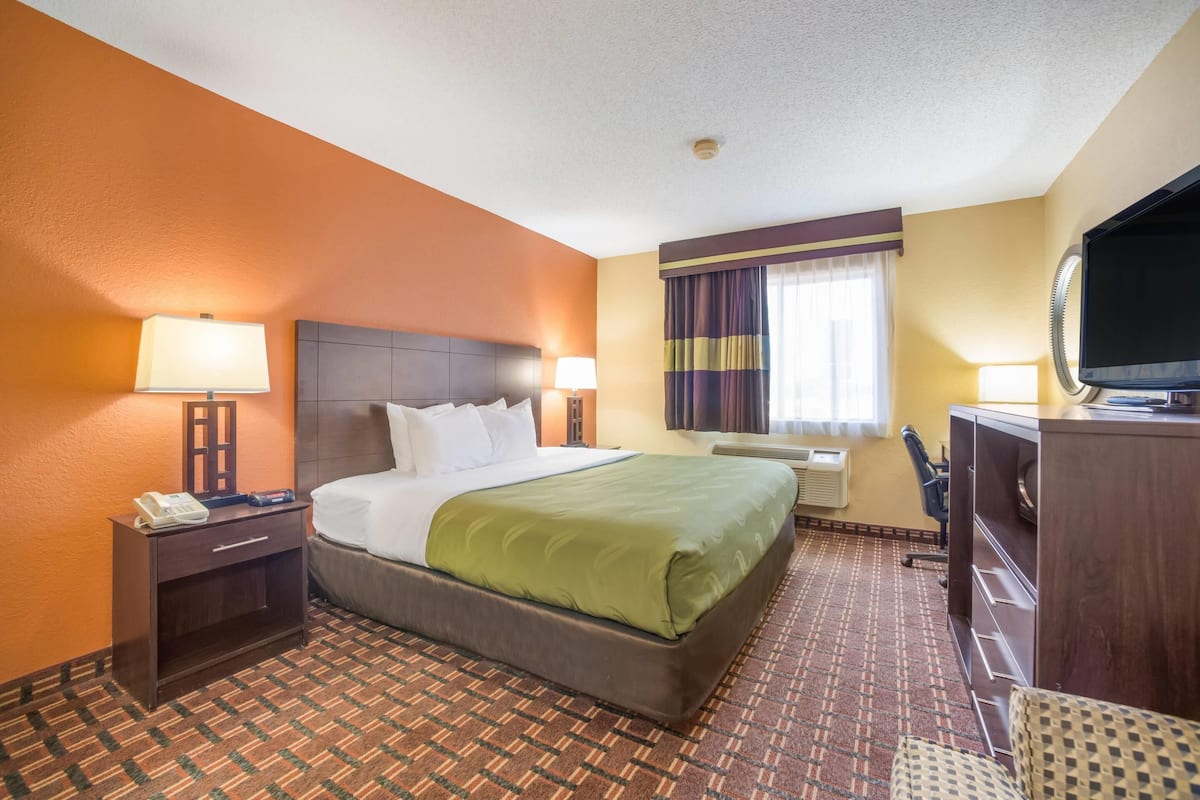 A hotel room with a large bed, two bedside lamps, a desk with a telephone, a television, and a window with curtains.