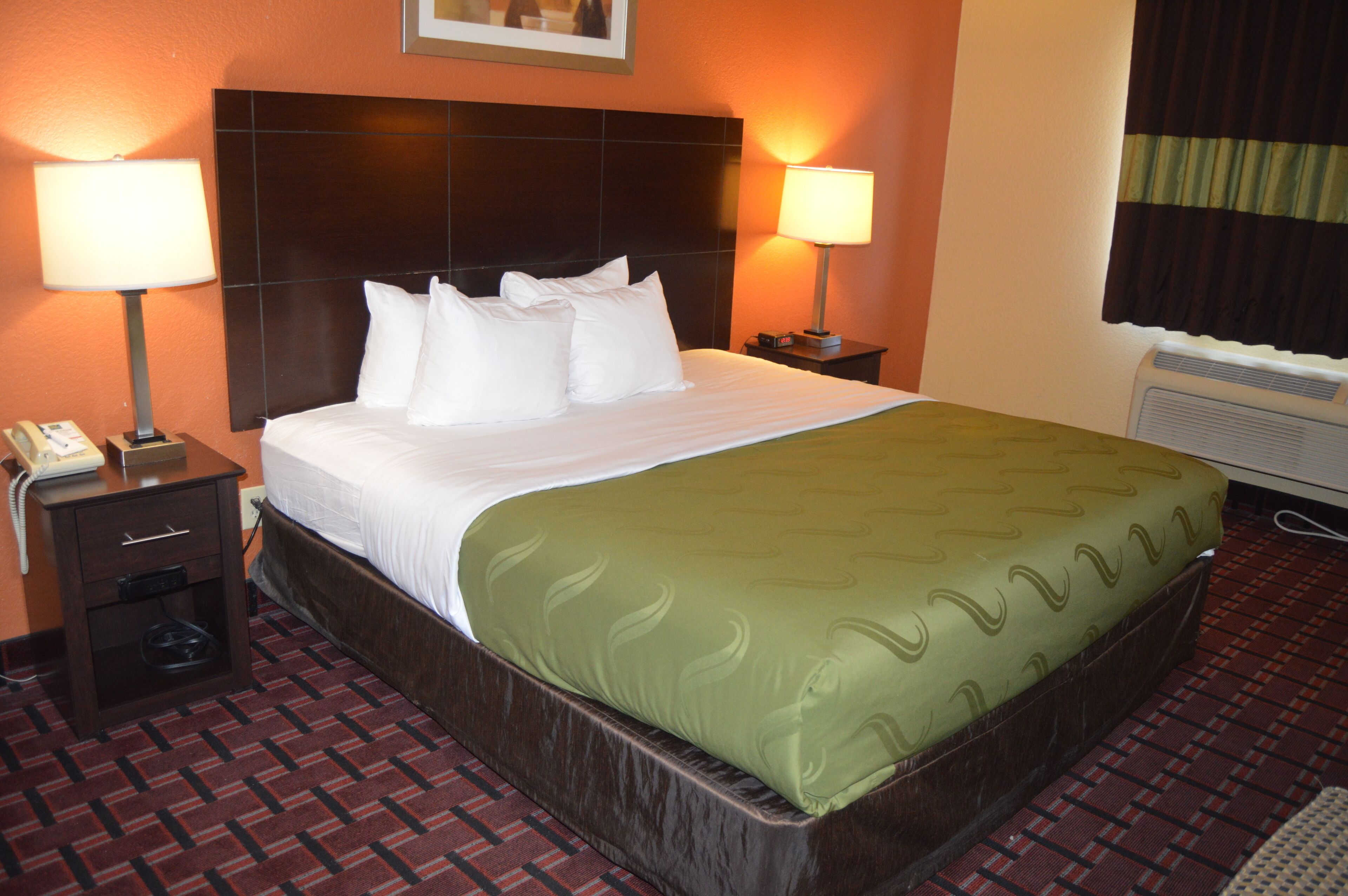A hotel room with a large bed, two bedside lamps, a telephone, and a heater.