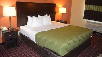 A hotel room with a large bed, two bedside lamps, a telephone, and a heater.