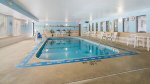 An indoor swimming pool with a mural of a beach scene on the walls, surrounded by white chairs and tables. - Quality Inn O'Fallon - St. Louis - Shiloh (O'Fallon)