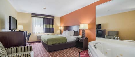 A hotel room with a bed, a desk with a computer, a chair, a large mirror, and a bathtub.