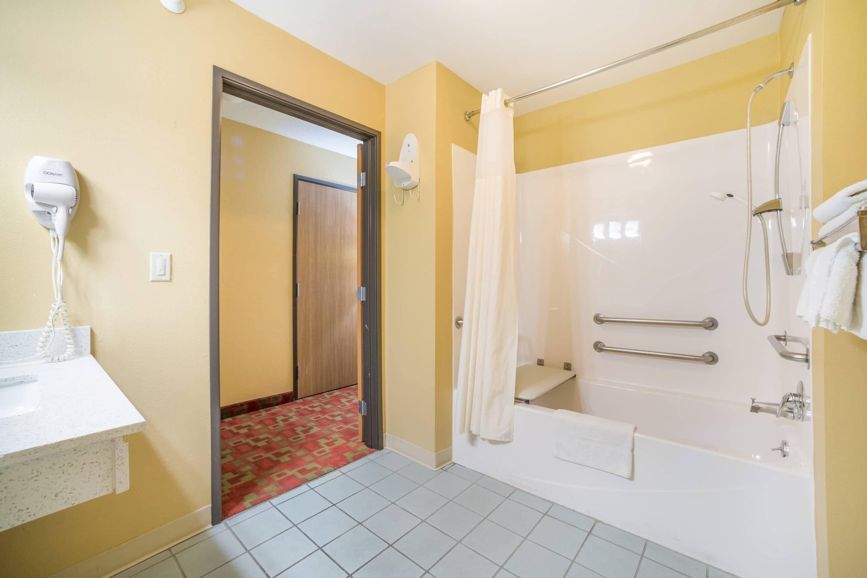 A bathroom with a shower, a bathtub, a hairdryer, and a towel rack.