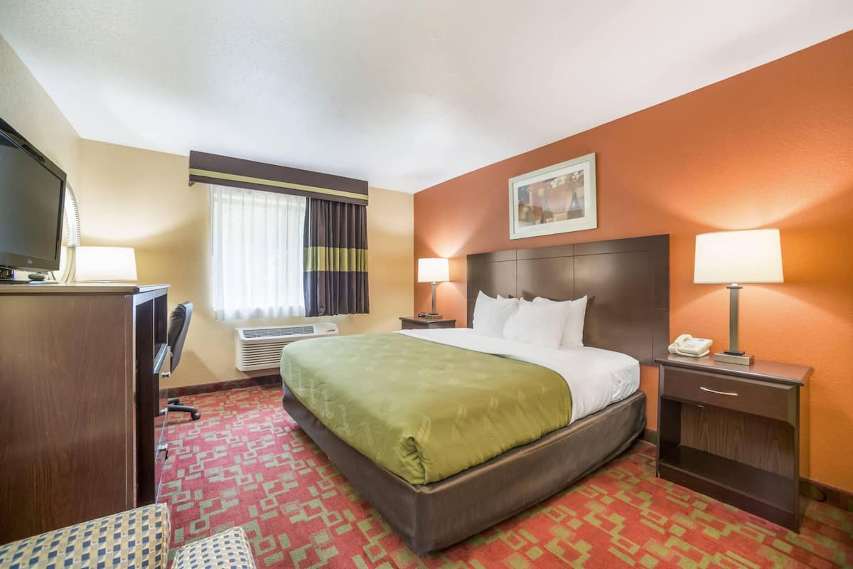 A hotel room with a large bed, two bedside lamps, a desk with a TV, and a window with curtains.