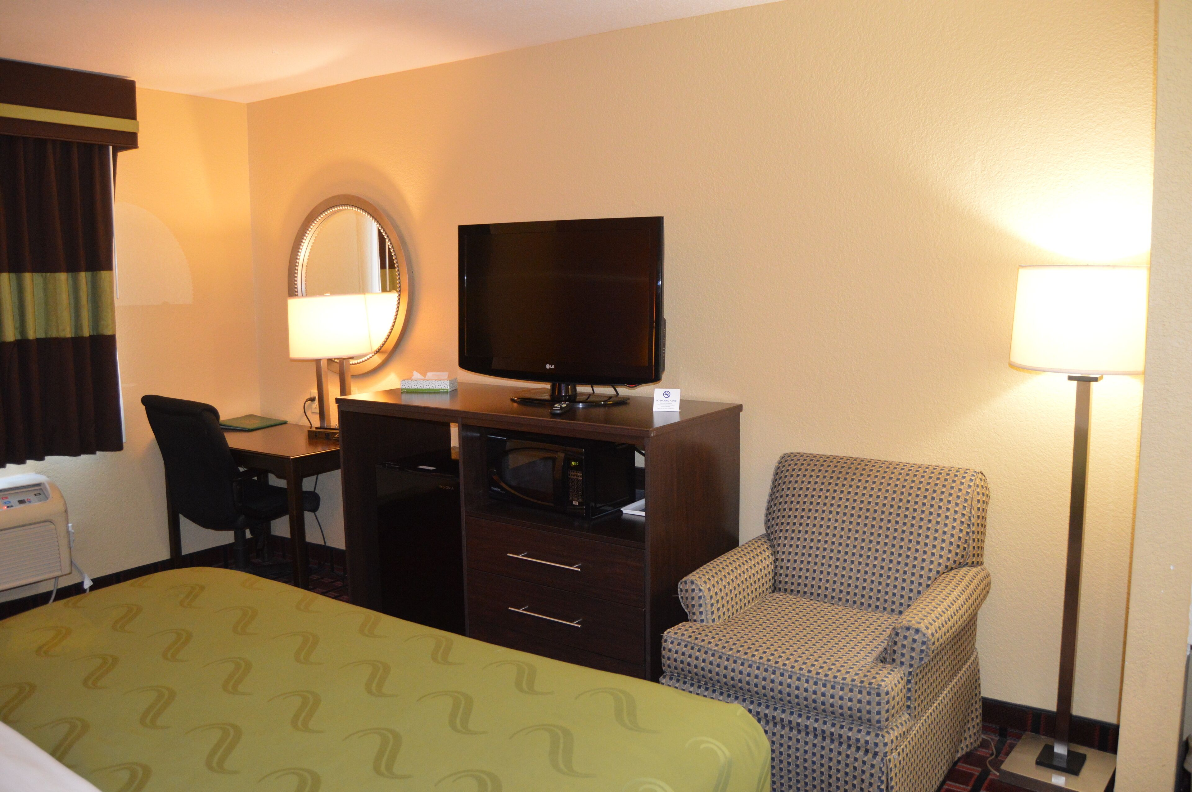 Una habitación de hotel con una cama, un escritorio con televisor, una silla y dos lámparas.