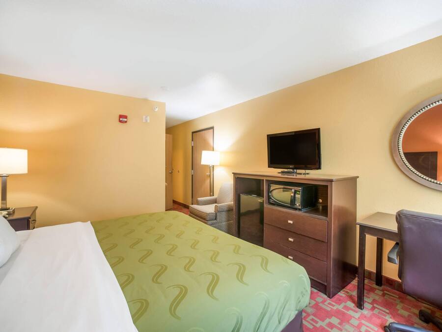 Een hotelkamer met een bed, een bureau, een stoel, een televisie, een dressoir en een spiegel.