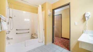 A bathroom with a bathtub, shower, and a hairdryer on the wall.