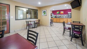 A restaurant with tiled floors, wooden tables and chairs, a counter with a TV, and a window with a view. - Quality Inn O'Fallon - St. Louis - Shiloh (O'Fallon)