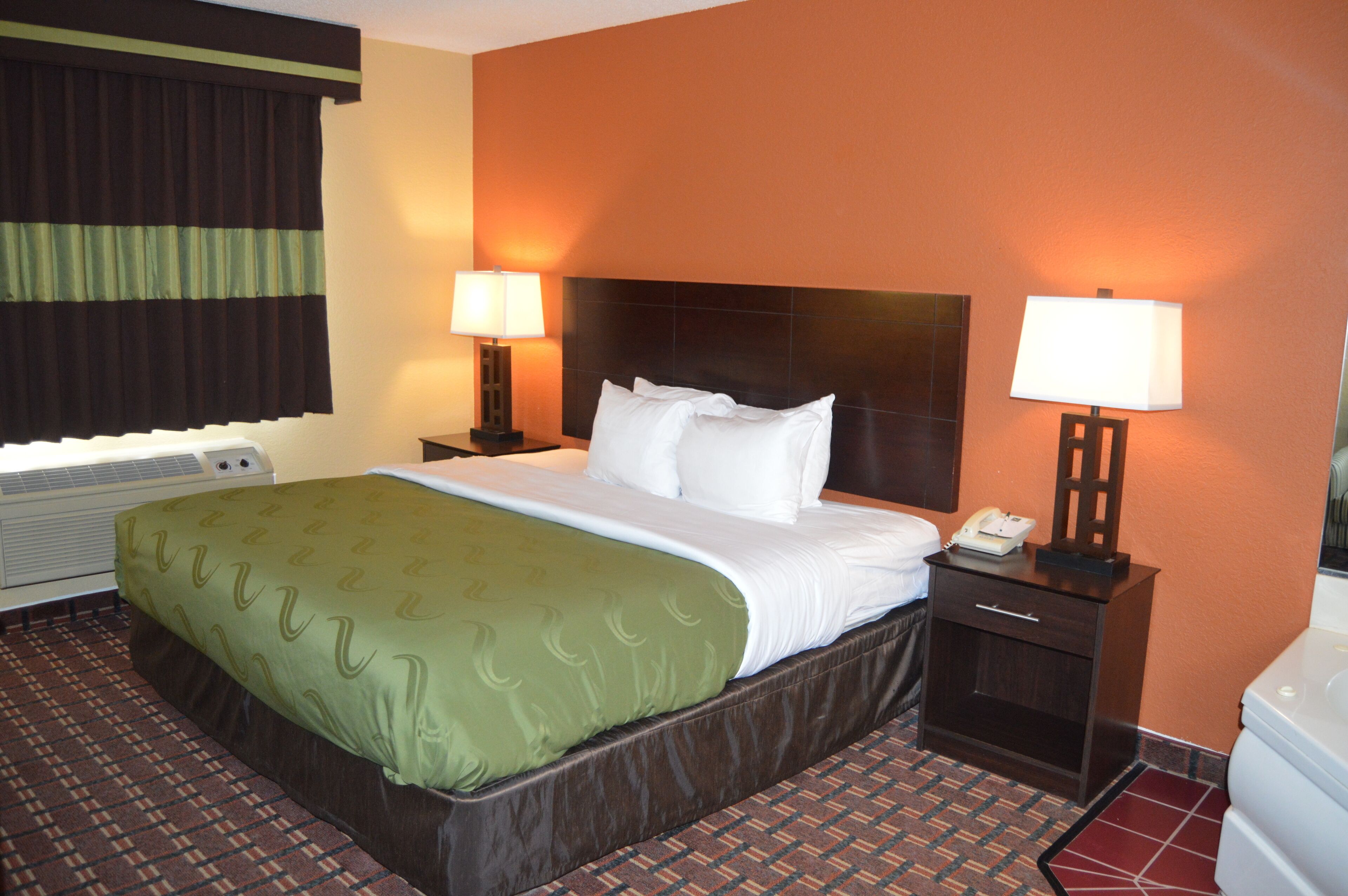 A hotel room with a large bed, two bedside tables with lamps, a heater, and a tiled floor.