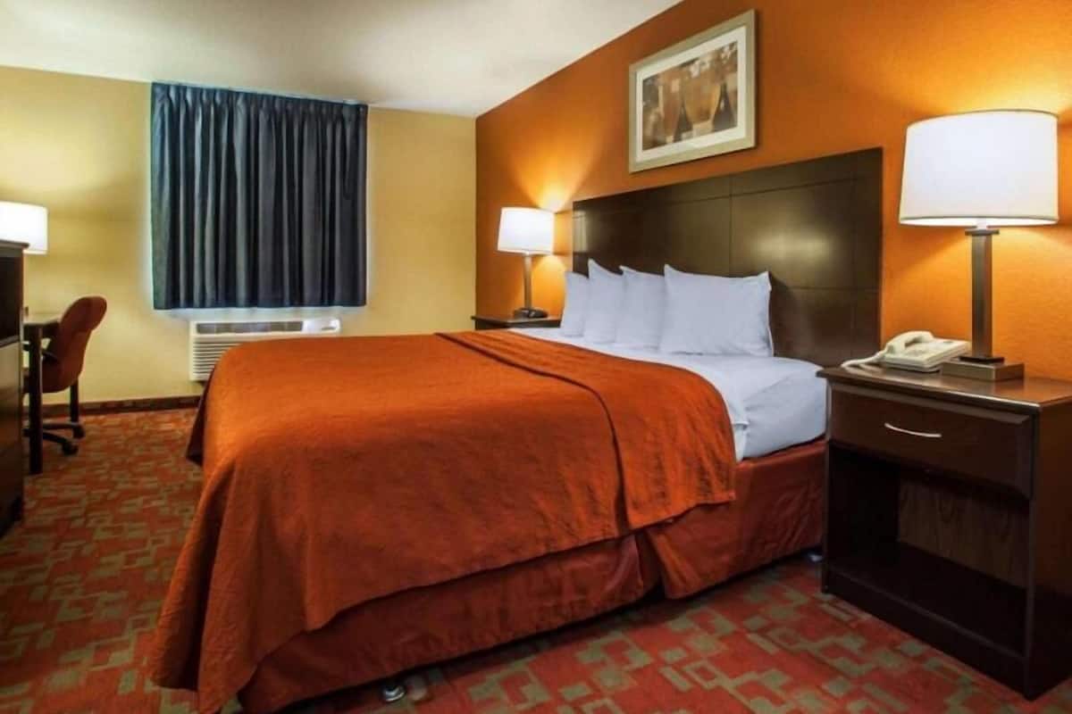 A hotel room with a bed, two bedside lamps, a desk with a telephone, a chair, and a window with curtains.