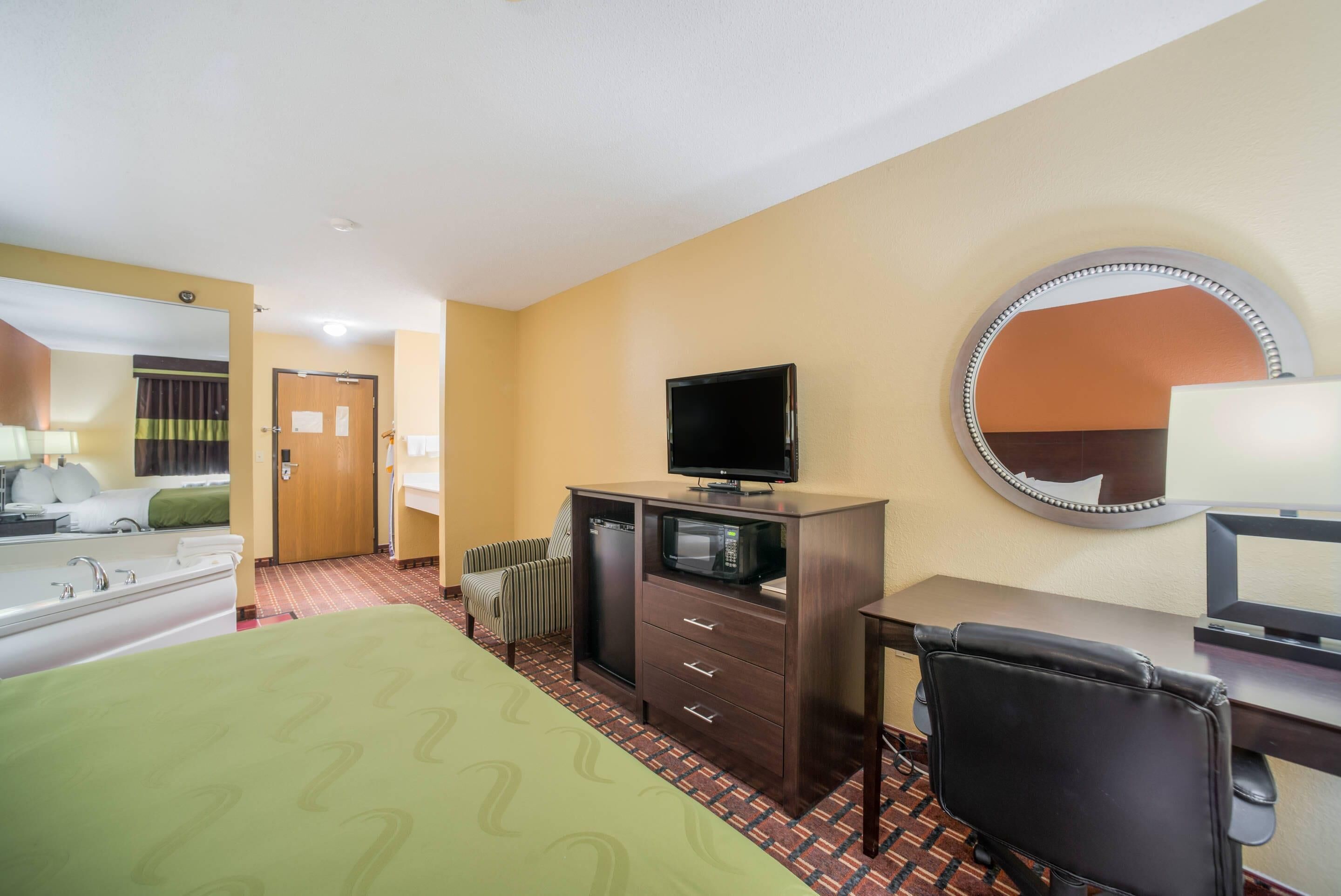 A hotel room with a bed, a desk, a television, a mirror, and a radiator.