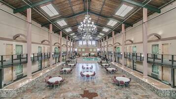 A spacious indoor atrium with a high ceiling, stone flooring, and multiple tables and chairs arranged for dining.