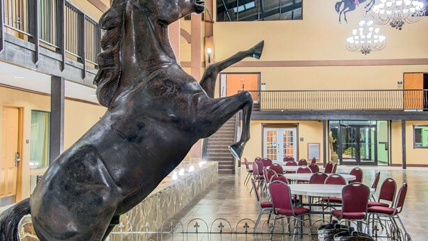 Amplio espacio interior con una gran escultura de bronce de un caballo, varias mesas de comedor con sillas rojas y una lámpara de araña.