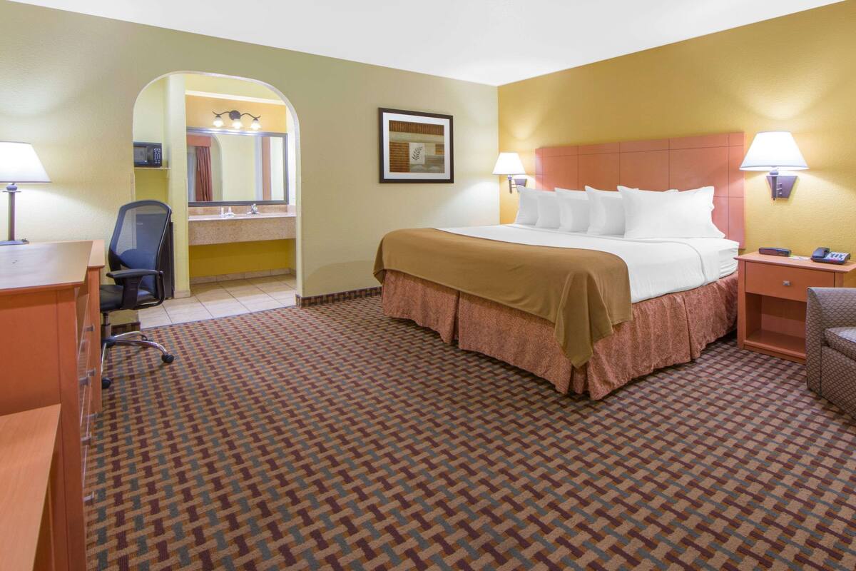 A hotel room with a bed, two bedside lamps, a desk with a chair, a mirror, and a framed picture on the wall.