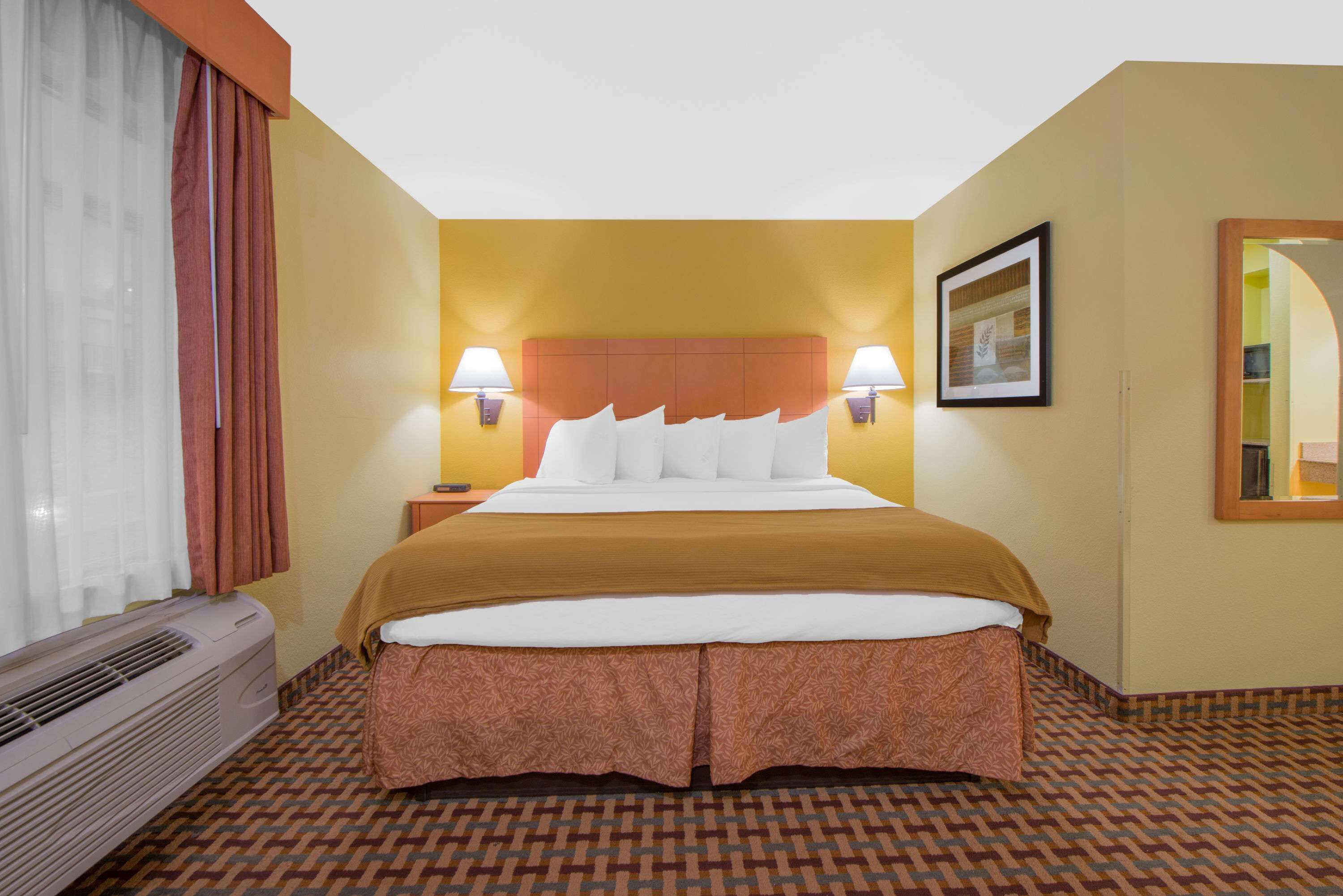 Habitación de hotel con cama, dos lámparas de noche, un cuadro en la pared y una ventana con cortinas.