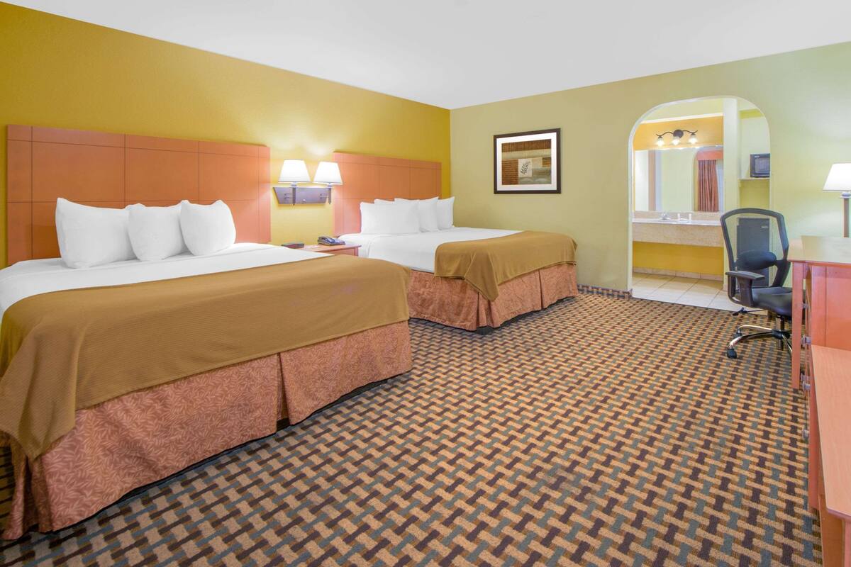 A hotel room with two beds, a desk, a chair, a mirror, and a patterned carpet.
