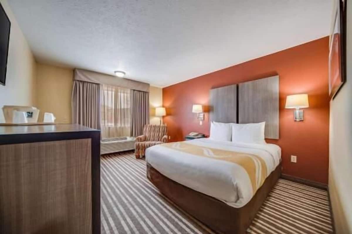 A hotel room with a bed, a desk, a chair, and two wall-mounted lamps.
