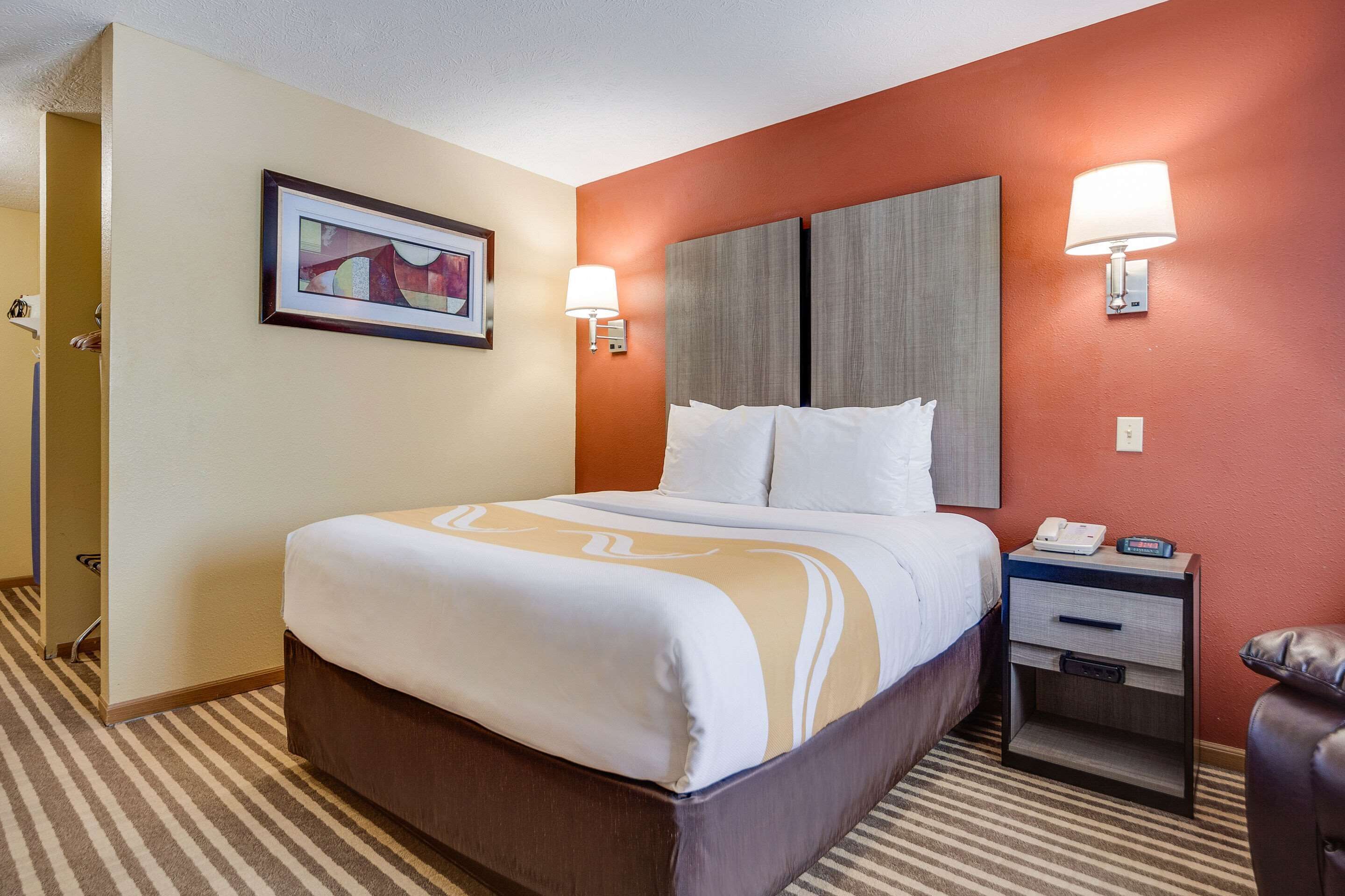 A hotel room with a bed, bedside table, lamp, and a framed picture on the wall.