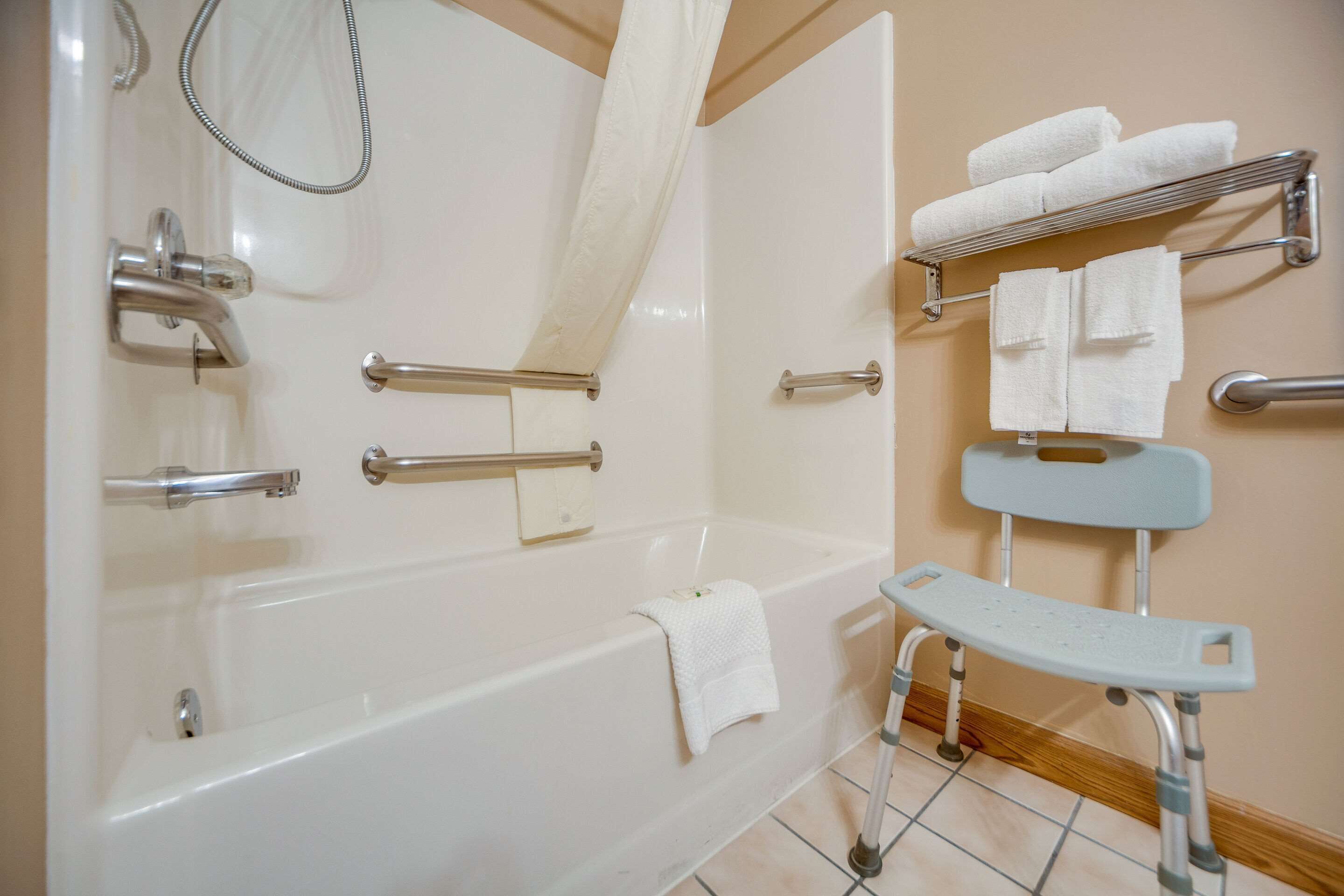 Un baño moderno con bañera, barras de apoyo, cabezal de ducha, toallero y un banco accesible en silla de ruedas.