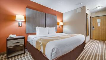 Una habitación de hotel con una cama grande, una mesita de noche, una lámpara y una puerta.