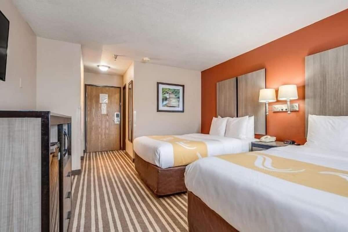 A hotel room with two beds, a desk, a telephone, and a wall-mounted lamp.