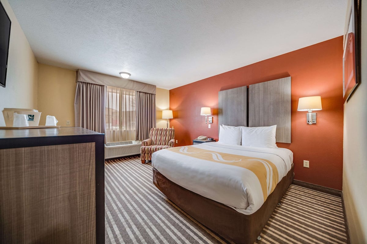 A hotel room with a large bed, a desk, two bedside lamps, a chair, and a window with curtains.