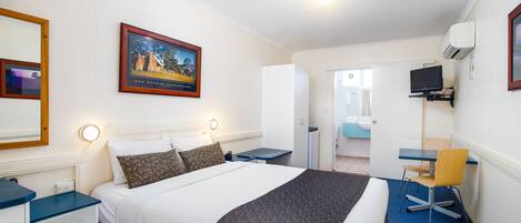 A hotel room with a bed, bedside tables, a desk with a chair, a television, and a framed picture on the wall.
