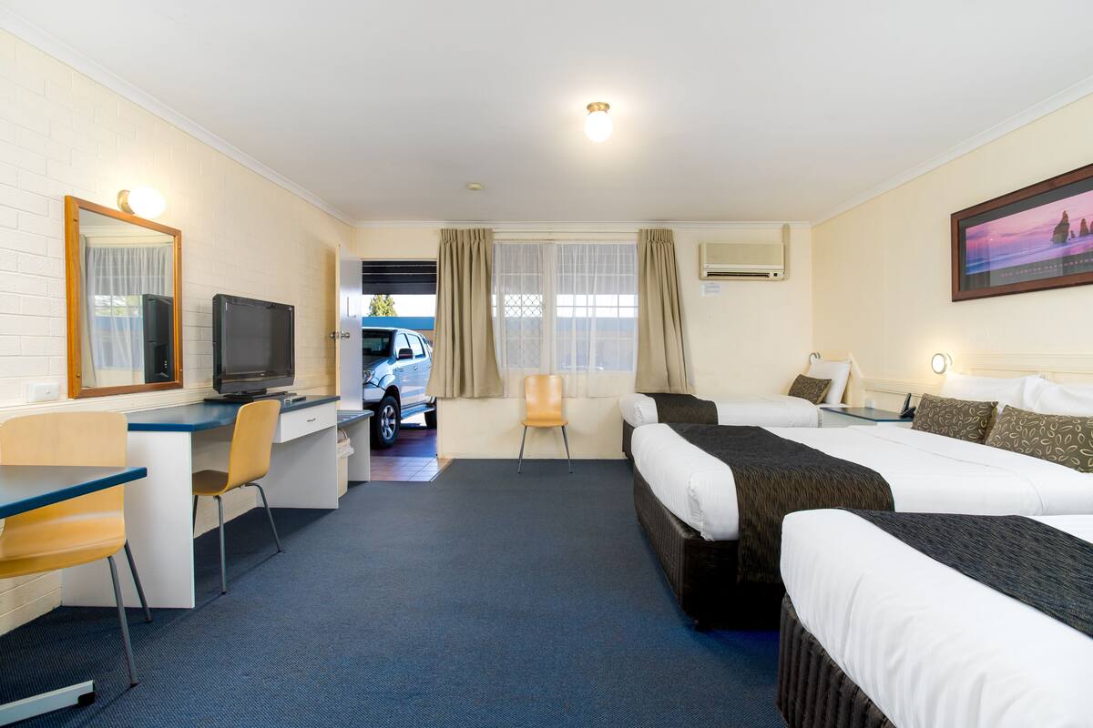 Habitación de hotel con dos camas, un escritorio con silla, un televisor y un coche estacionado afuera.