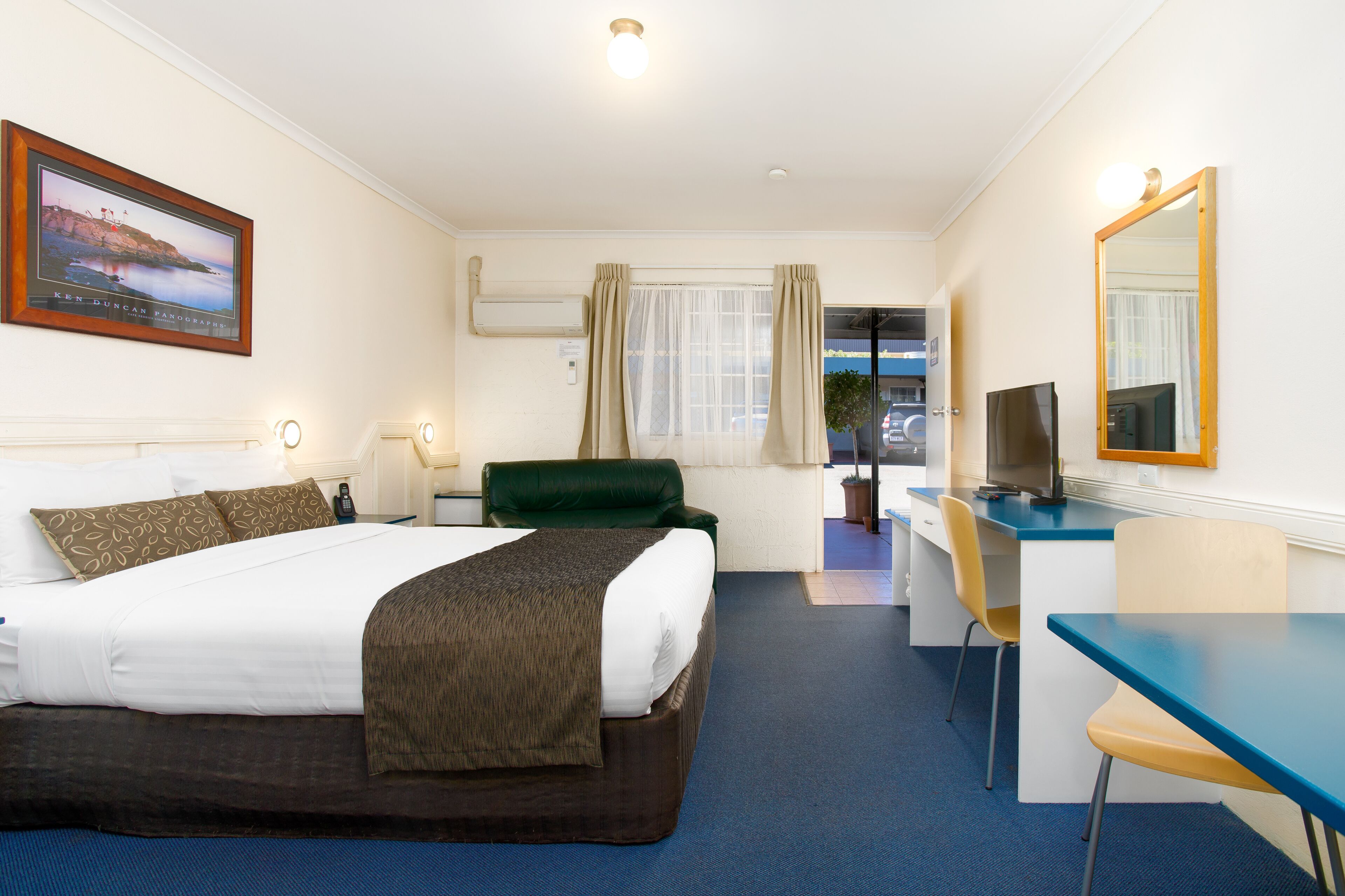 Habitación de hotel con una cama grande, un escritorio con silla, un televisor y una ventana con cortinas.