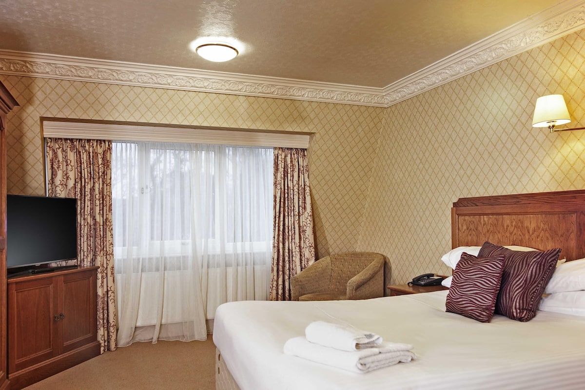 A hotel room with a bed, a TV, a chair, a desk, and a lamp.