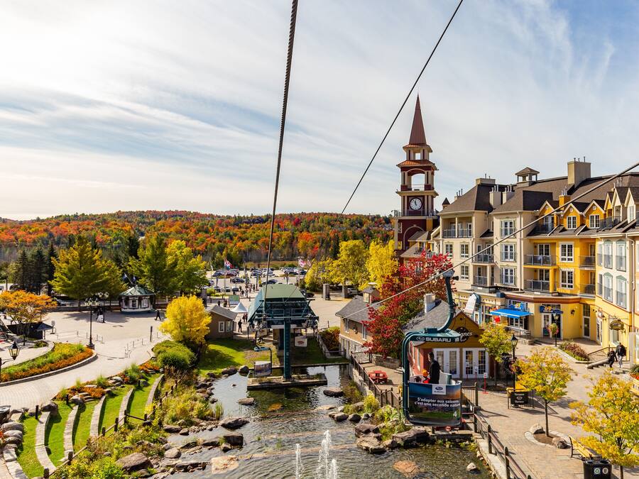 A town square with a central fountain, surrounded by buildings with a clock tower, and a backdrop of autumn-colored trees.