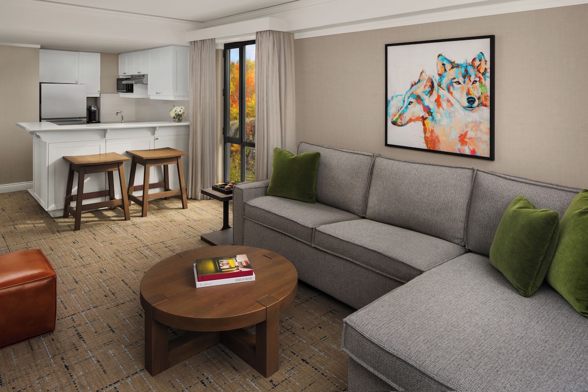 A modern living room with a grey sofa, wooden coffee table, and a kitchen area in the background.
