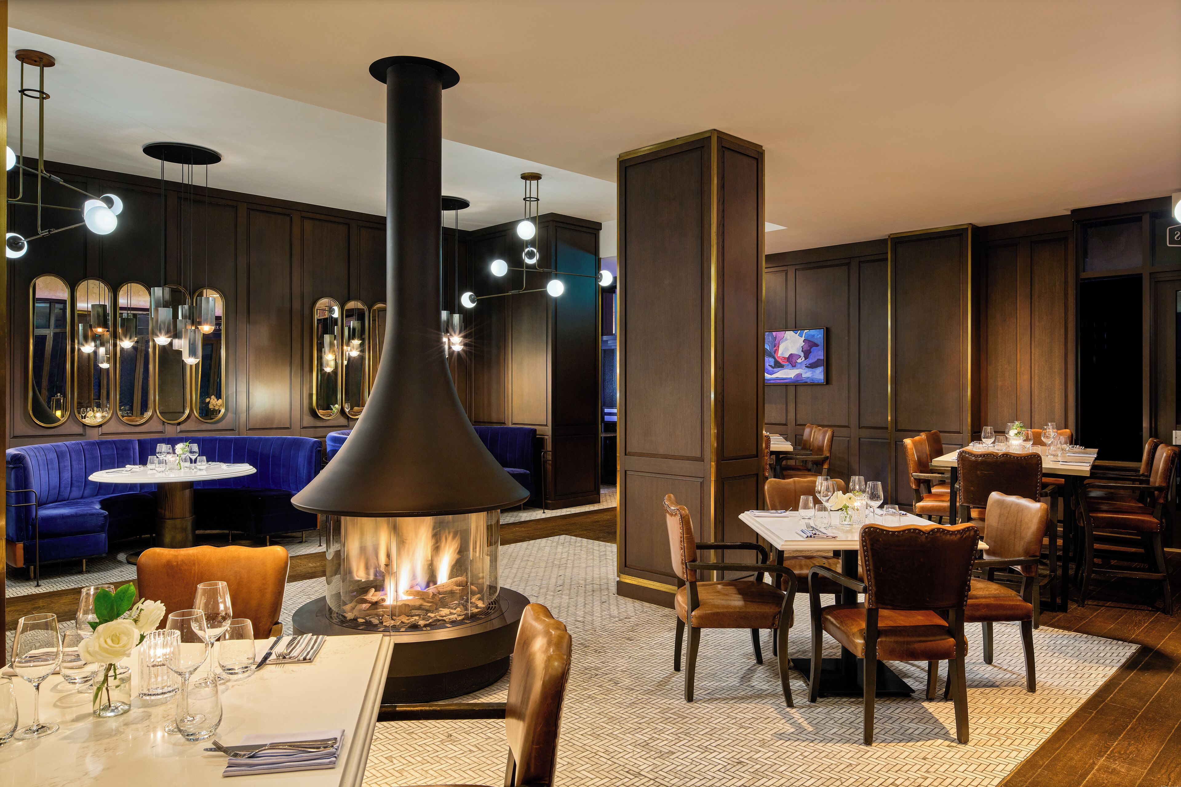 Un restaurant doté d’un poêle à bois central, de tables rondes et de coins salons bleus.
