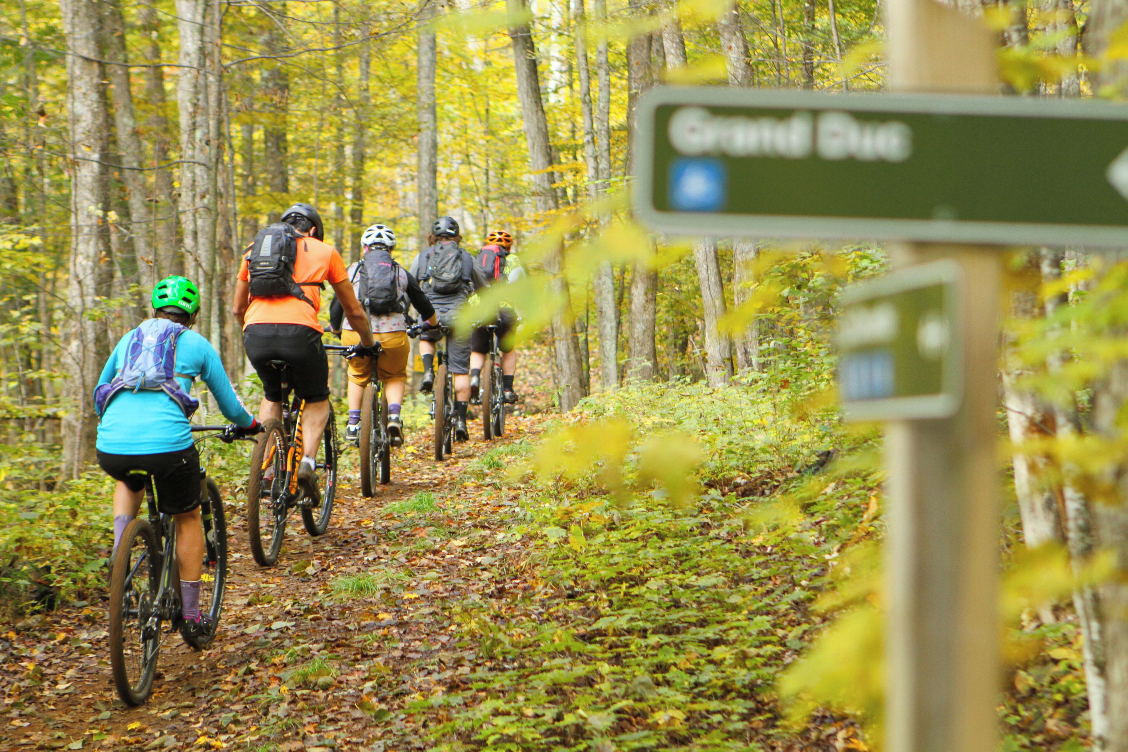 A group of cyclists on a forest trail with a sign indicating the direction to Grand Duke.