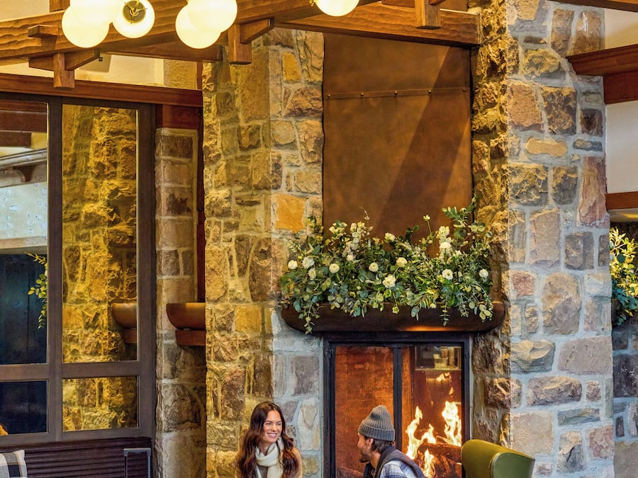 A stone fireplace with a fire, a green armchair, and a bench with a suitcase and a bag.