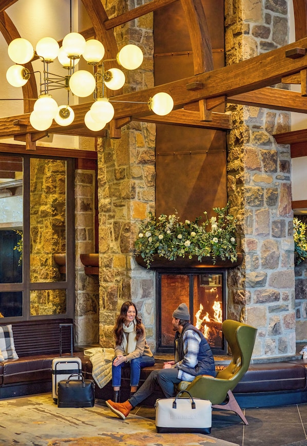 A stone fireplace with a fire, a green armchair, and a bench with a suitcase and a bag.