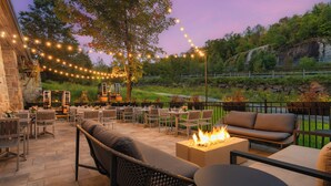 An outdoor patio with tables and chairs, string lights, a fire feature, and a view of a natural landscape. - Fairmont Tremblant (Mont-Tremblant)