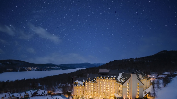 A snow-covered hotel with a large building, a swimming pool, and a view of a snowy landscape under a starry night sky. - Fairmont Tremblant (Mont-Tremblant)